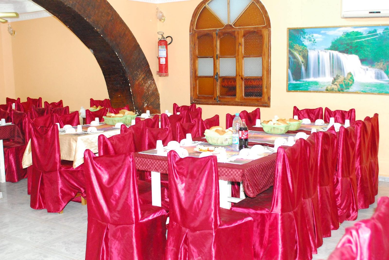 La grande salle vo&ucirc;t&eacute;e, tables rondes et housses de chaise rouge bordeaux